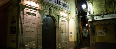 Una calle estrecha con un edificio que tiene una puerta negra grande y un balcón con barandillas de metal decorativo.