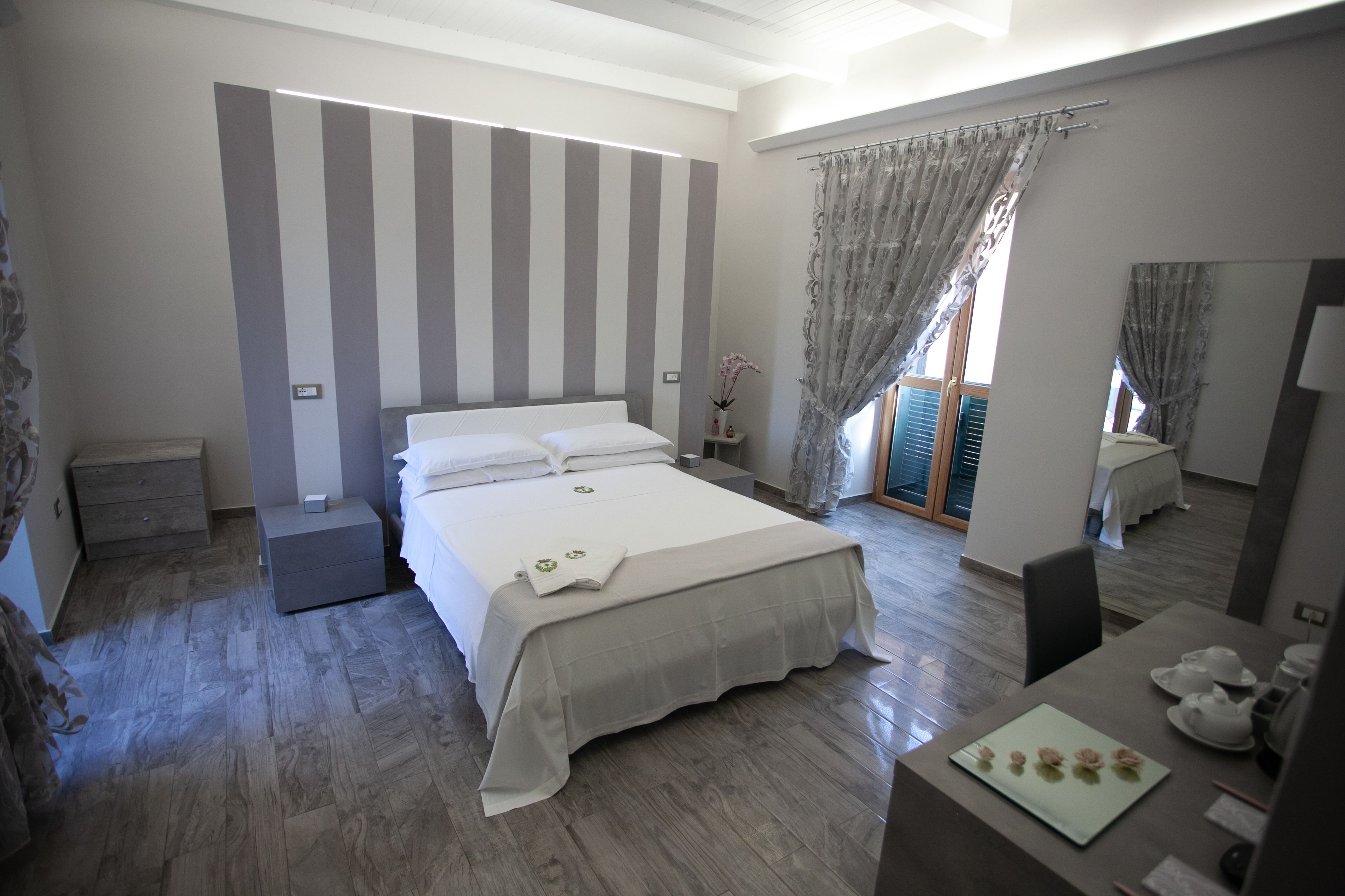 A bedroom with a large bed, a bedside table, a desk with a chair, and a window with curtains.