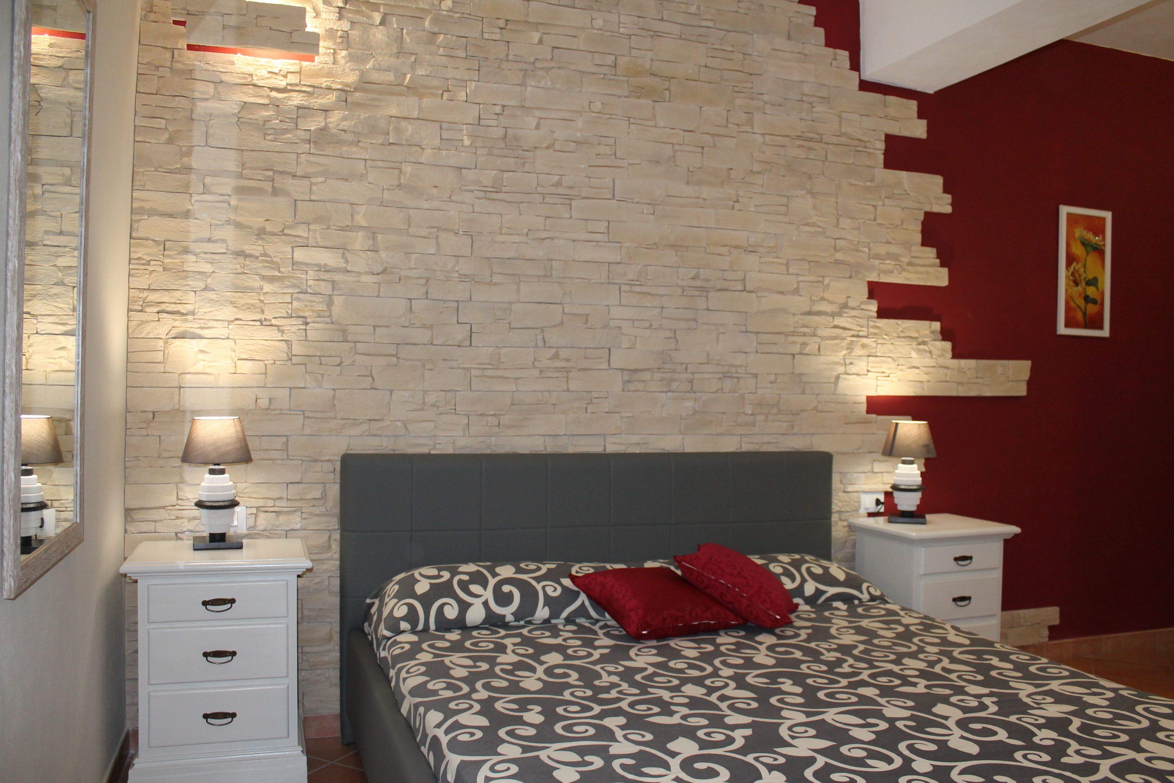 A bedroom with a stone-patterned wall, a bed with patterned bedding, and bedside lamps.