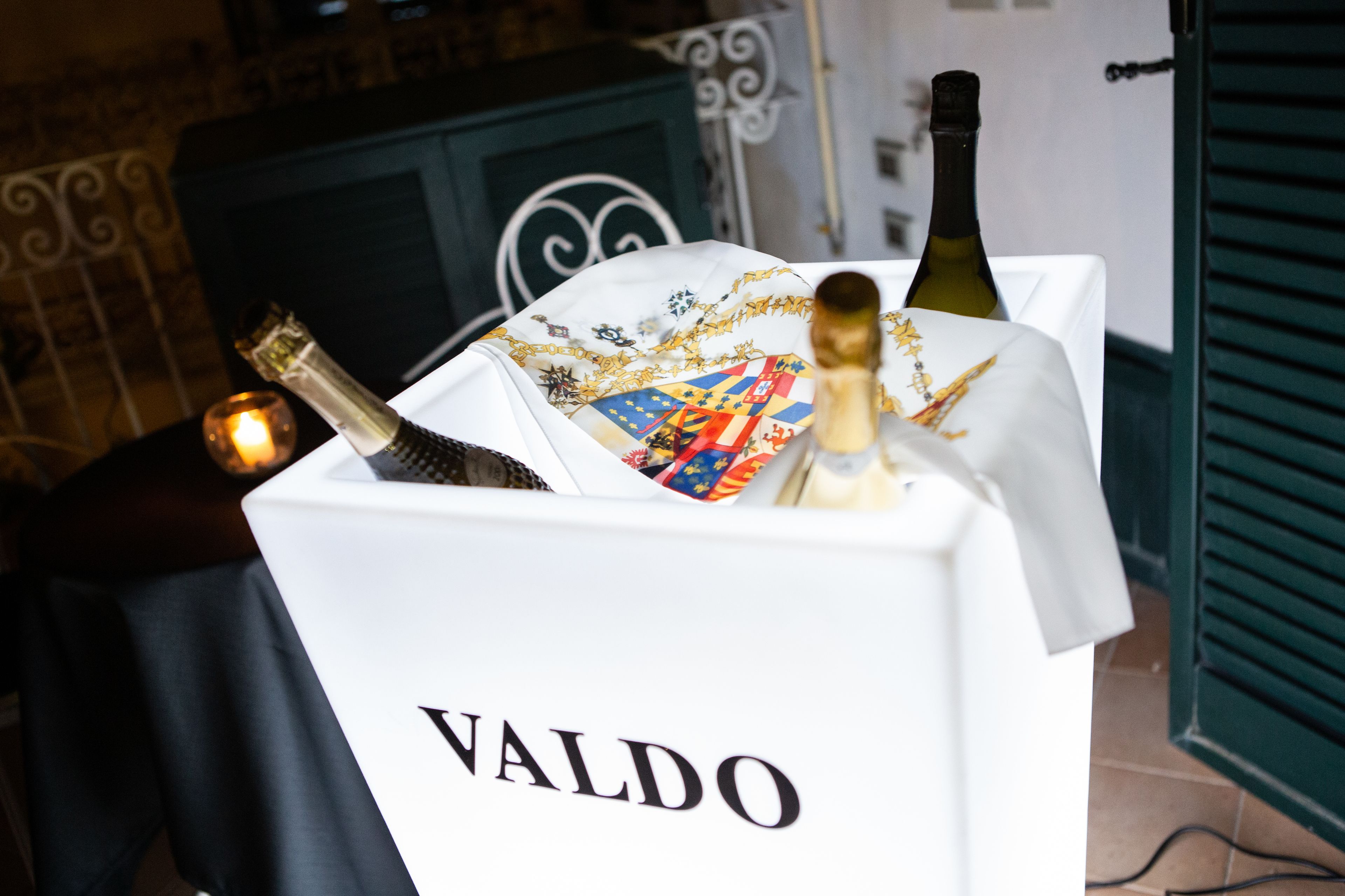 A minibar with a bottle of Valdo wine, a bottle of champagne, and a decorative cloth.