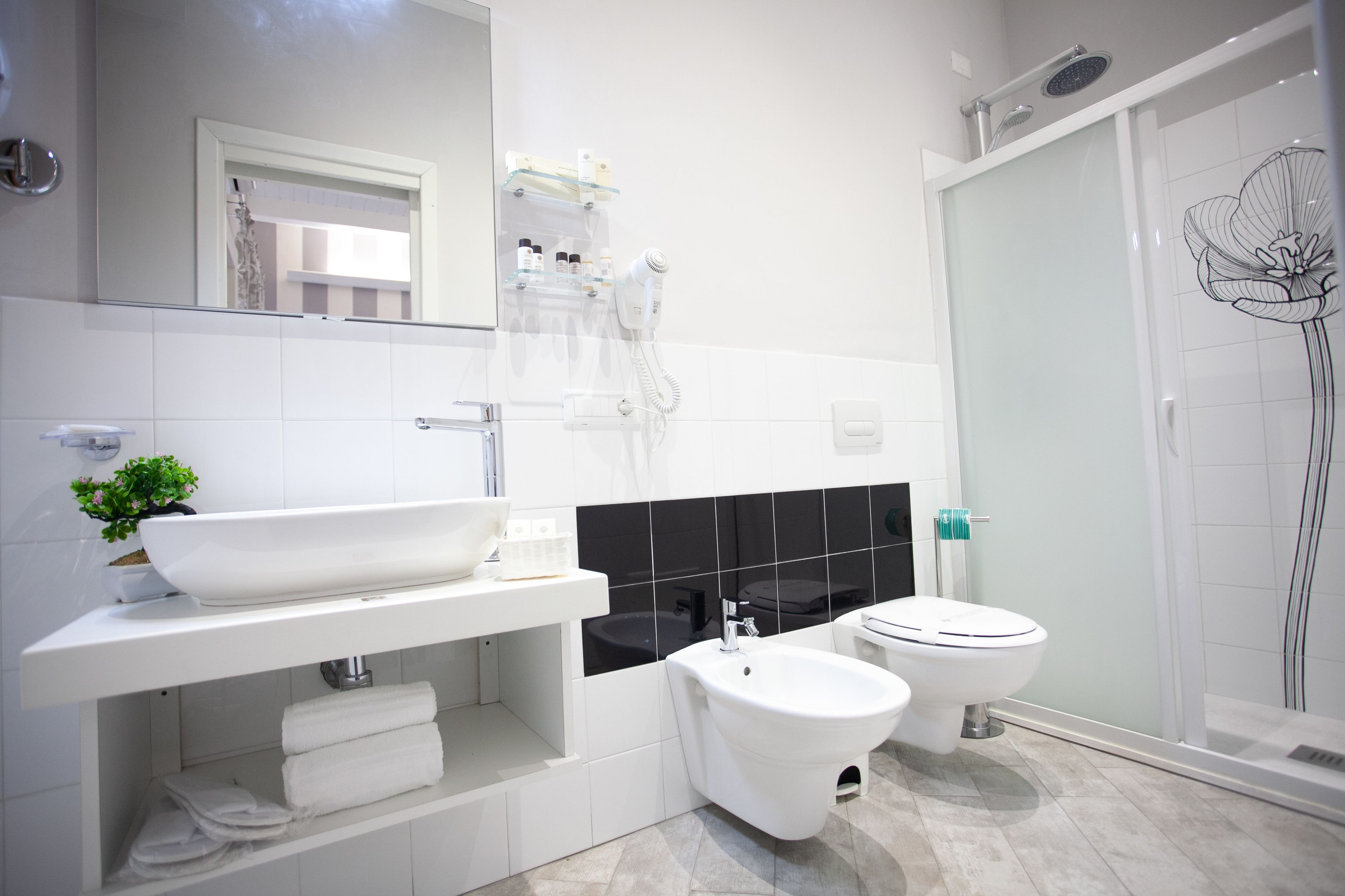 Un baño moderno con un lavamanos grande blanco, un bidé, un inodoro y una cabina de ducha de vidrio.