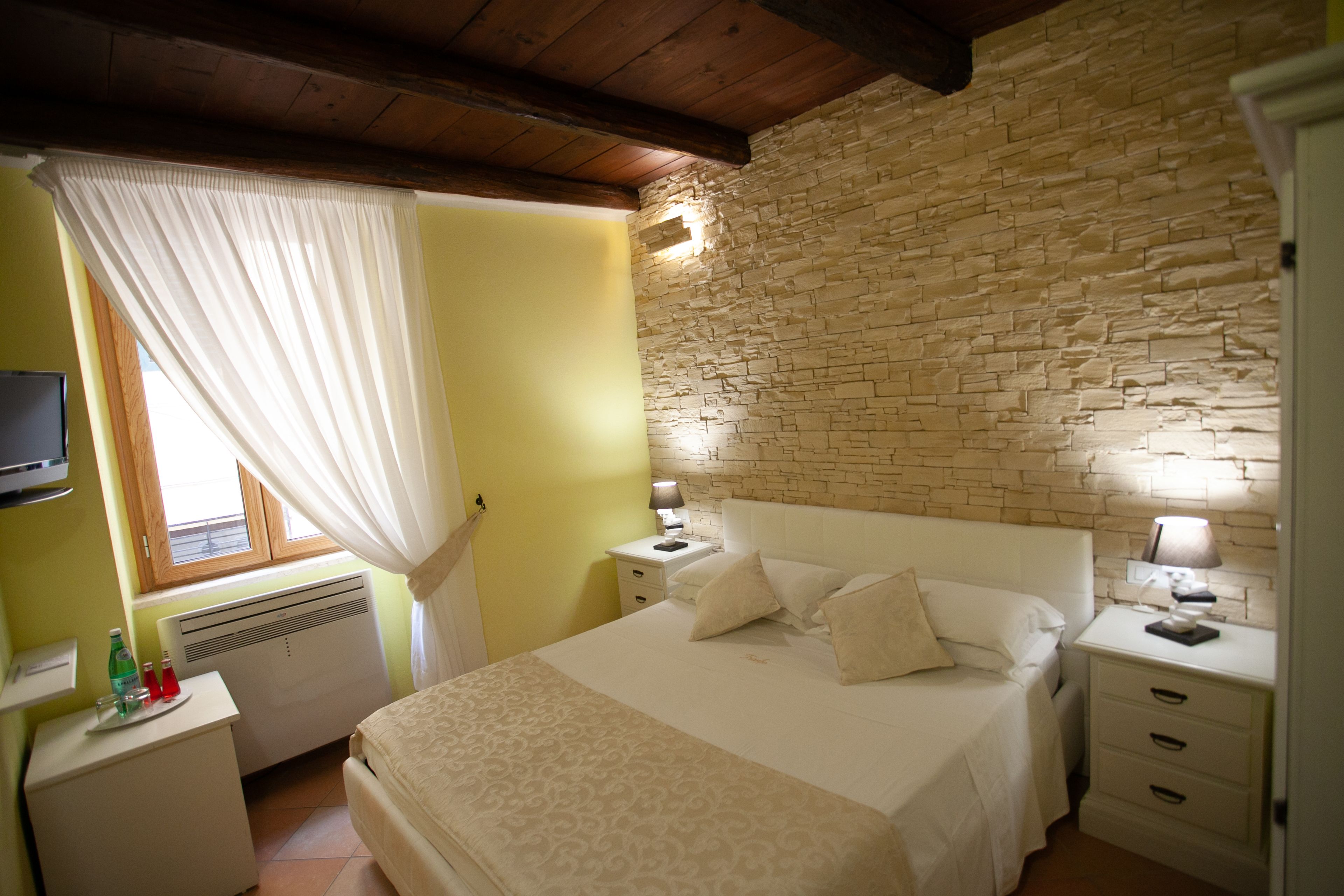 A bedroom with a bed, two bedside tables, a TV, and a stone wall.