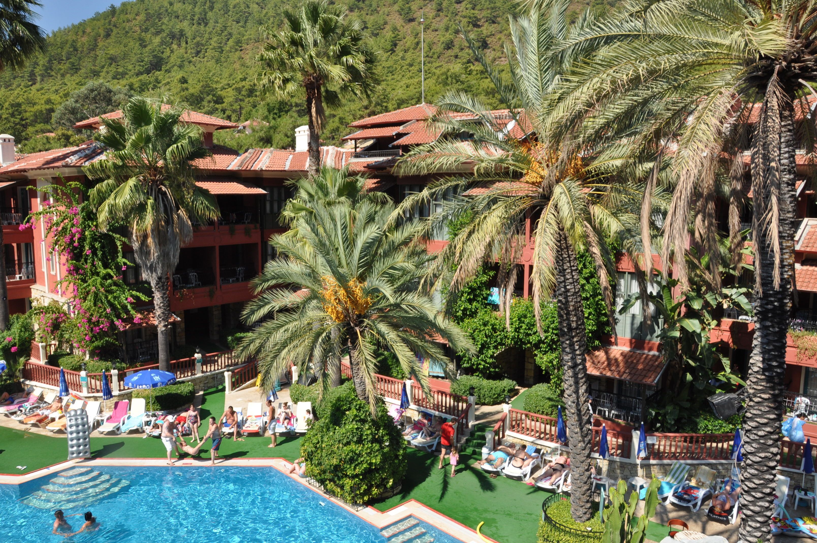 A resort with a swimming pool, palm trees, and a mountainous backdrop.