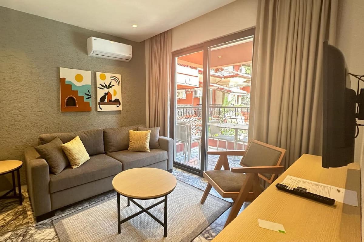 A modern living room with a grey sofa, two small tables, and a large window with a view of buildings.