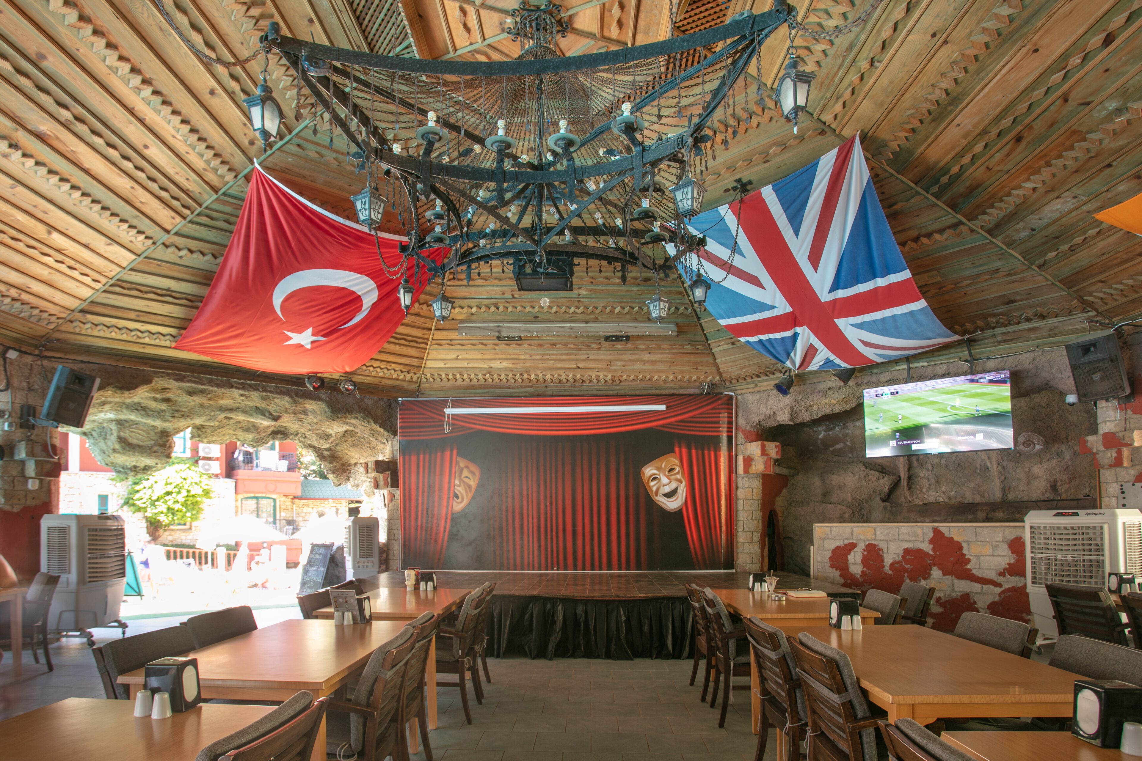 A restaurant with a stage, flags, and a television screen.