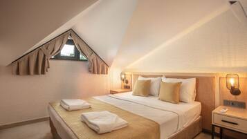 Ein Hotelzimmer mit schrägverdeckter Decke, einem Bett mit gemusterten Betttextilien, zwei Nachttischlampen und einem Nachttisch.