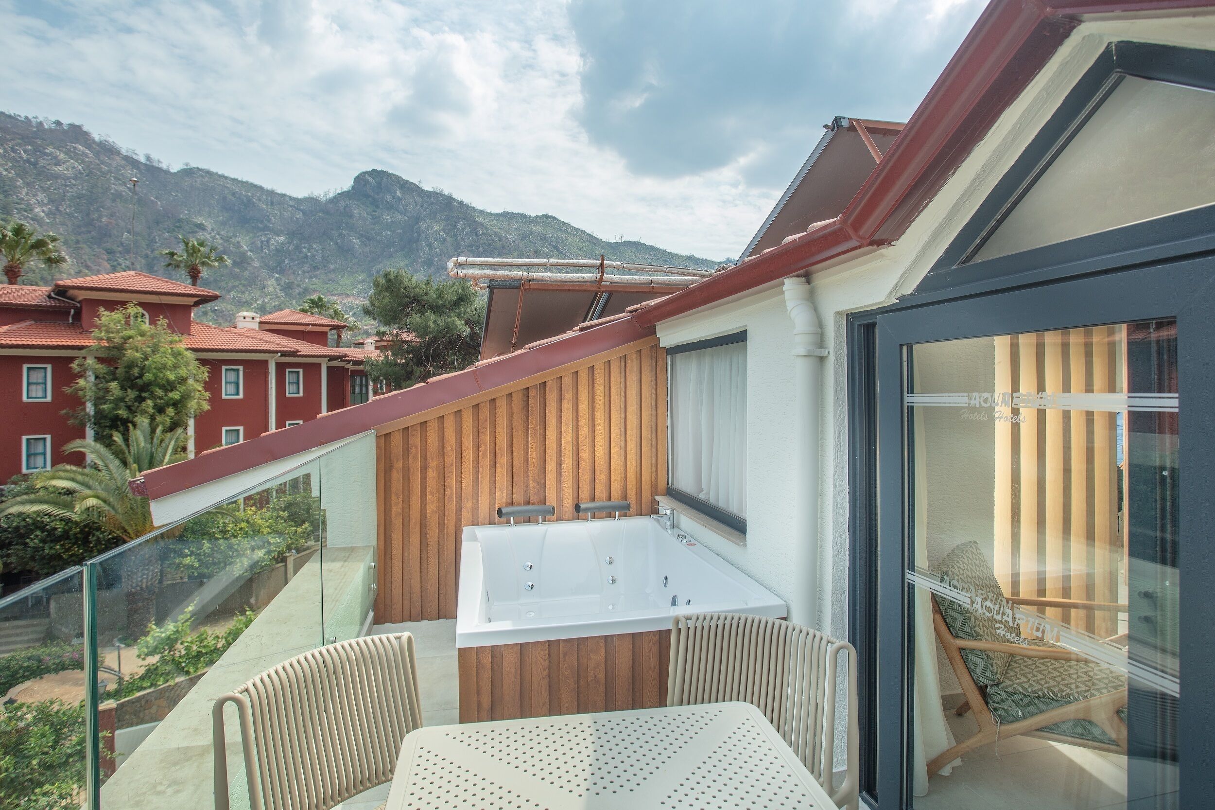 A balcony with a glass railing, a wooden slatted wall, a white bathtub, and a table with chairs.