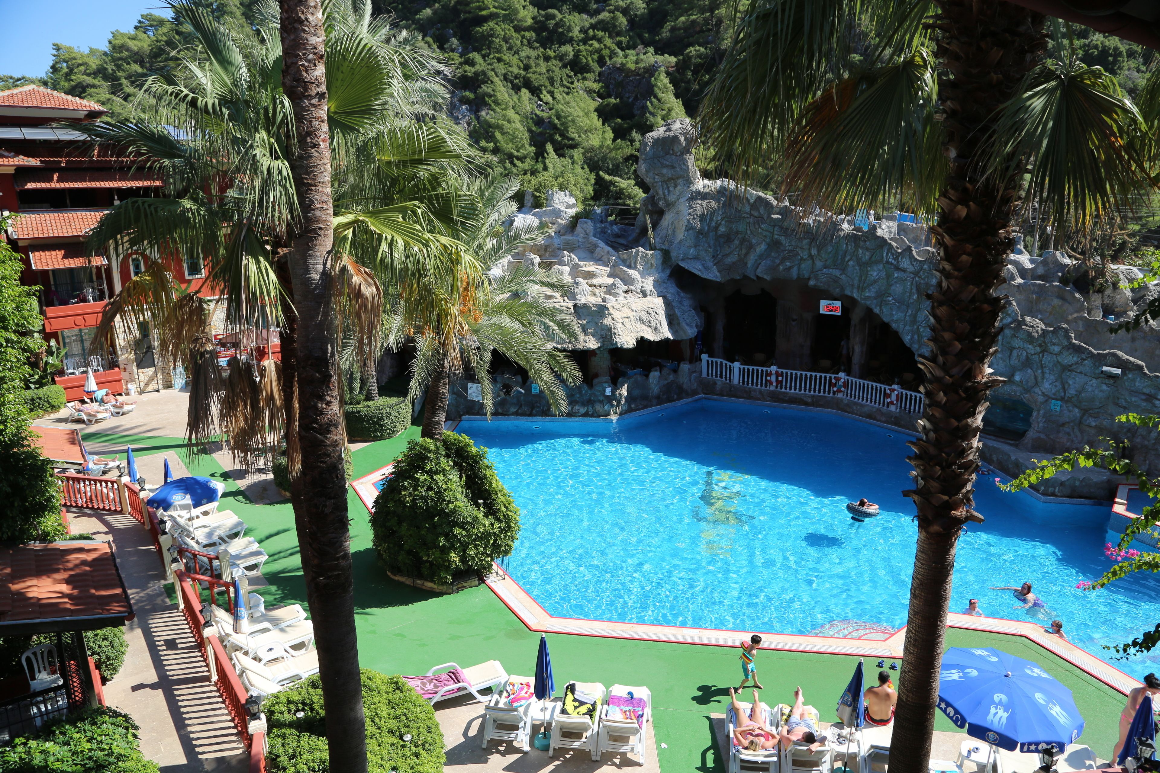 A pool area with lounge chairs, palm trees, and a rocky backdrop.