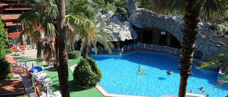A pool area with lounge chairs, palm trees, and a rocky backdrop.