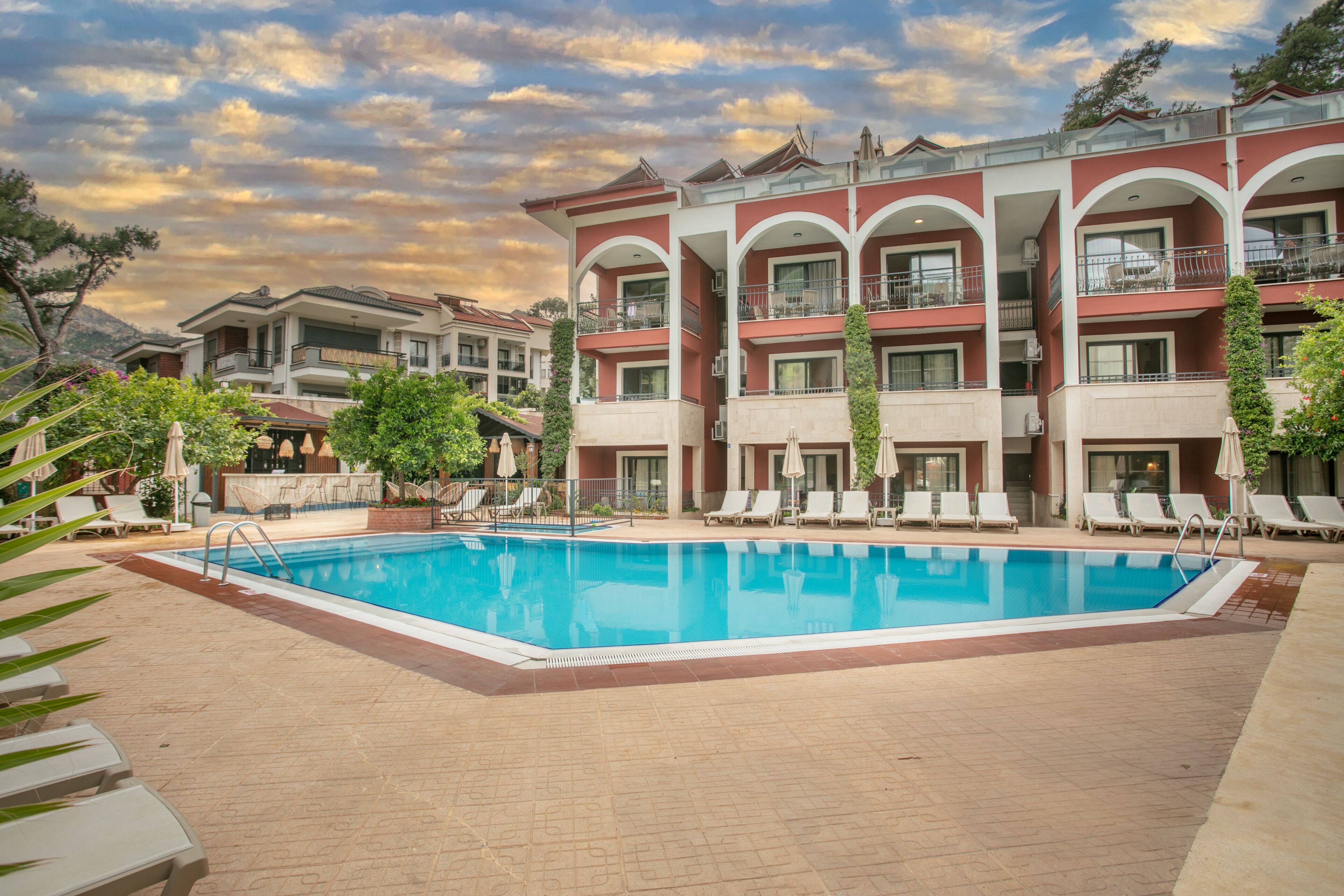 Un hotel con piscina circondata da sdraio e ombrelloni, con alle spalle un paesaggio montuoso.