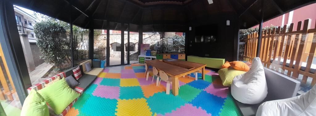 A cozy indoor space with a wooden table, colorful floor mats, and seating areas.