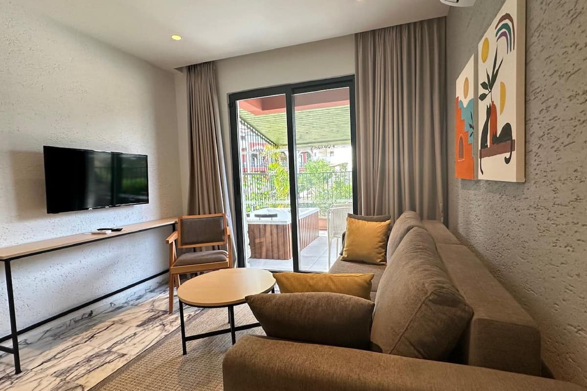 A modern hotel room with a flat-screen TV, a sofa, a small table, and a balcony with a hot tub.