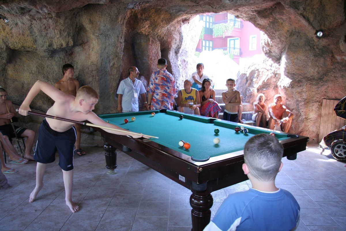 A pool table in a room with a stone wall and a view of buildings outside.