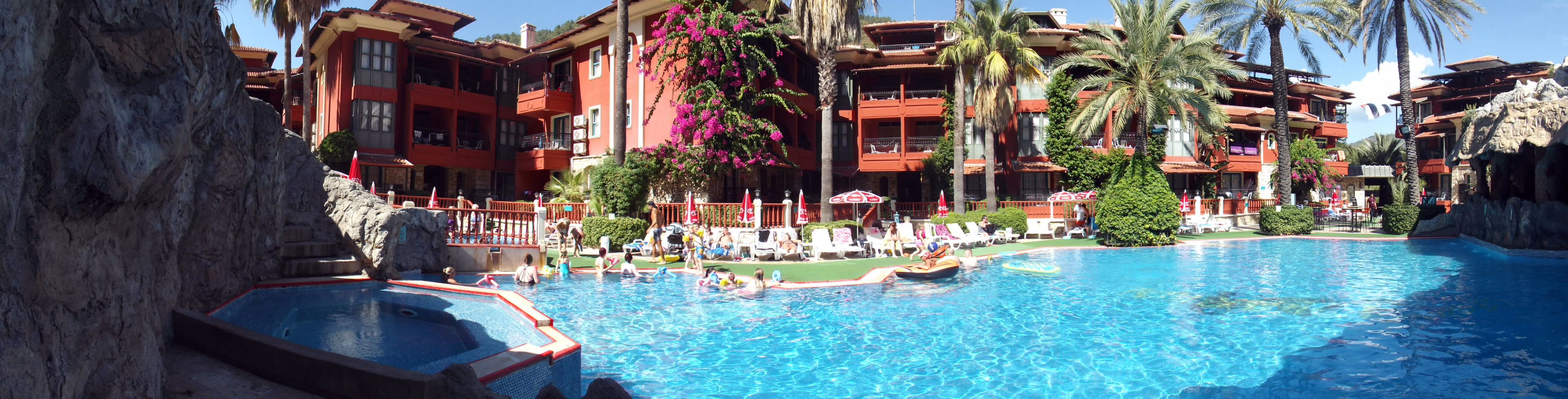 A hotel with a large pool, multiple balconies, and tropical landscaping.