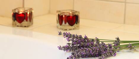 A bathroom with two glass cubes containing red heart-shaped candles and a bunch of lavender flowers on a white surface.