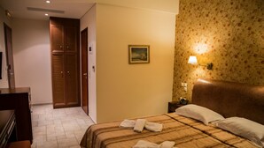 A hotel room with a bed, a nightstand, a lamp, a painting on the wall, and a wooden wardrobe. - Tesoro Hotel (Lefkada)