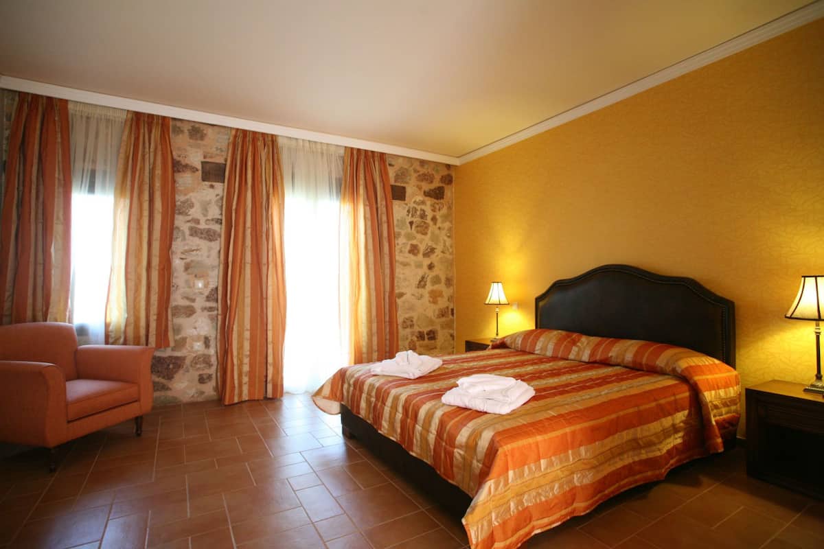 A hotel room with a bed, a chair, and a stone wall.