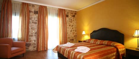 A hotel room with a bed, a chair, and a stone wall.