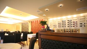 A hotel lobby with a reception desk, dining area, and a wall of wine bottles. - Tesoro Hotel (Lefkada)