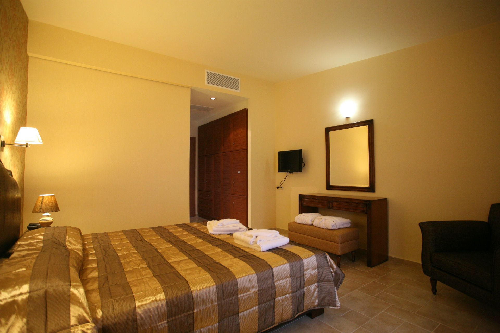 Una camera d'albergo con un letto, un comodino, una televisione, uno specchio e una sedia.