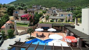 A pool area with lounge chairs and umbrellas, surrounded by hillside buildings and greenery. - Tesoro Hotel (Lefkada)