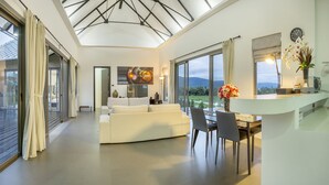 Una sala de estar moderna con un sofá blanco, una mesa de comedor y sillas. Hay un ventanal con vistas al exterior.