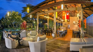 Un área de comedor al aire libre con mobiliario de mimbre y una zona de estar techada.