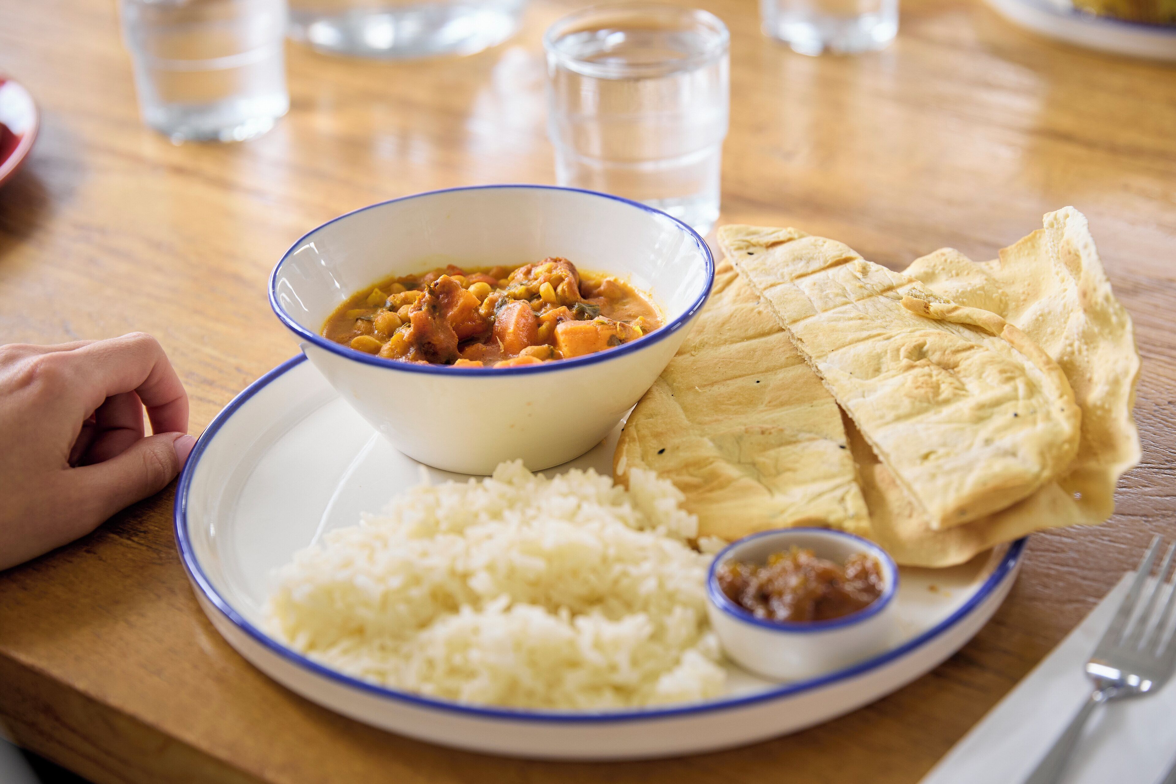 A plate with rice, a bowl of stew, flatbread, and a small bowl of sauce.