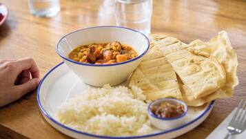 A plate with rice, a bowl of stew, flatbread, and a small bowl of sauce.