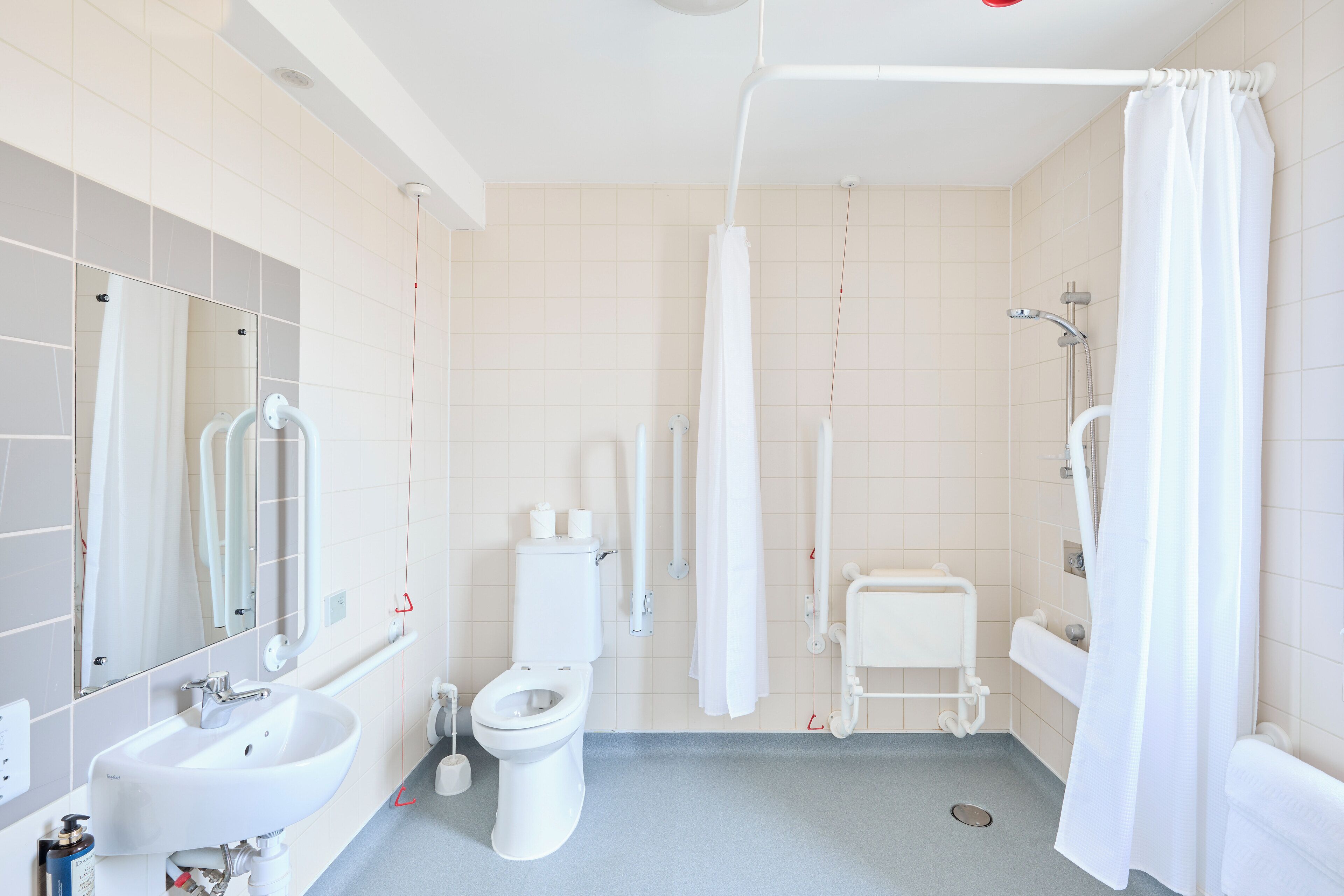 A modern bathroom with a sink, toilet, and shower area, featuring white fixtures and a tiled floor.