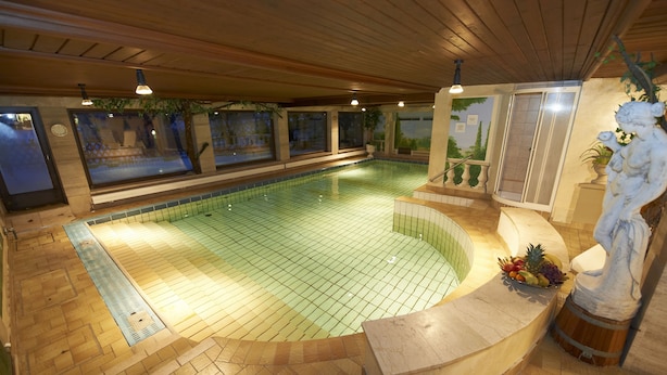 A swimming pool with a tiled floor, surrounded by wooden walls and a wooden ceiling. There is a statue of a lion holding a plant on the right side. - Landhaus Steiner (Altenmarkt im Pongau)