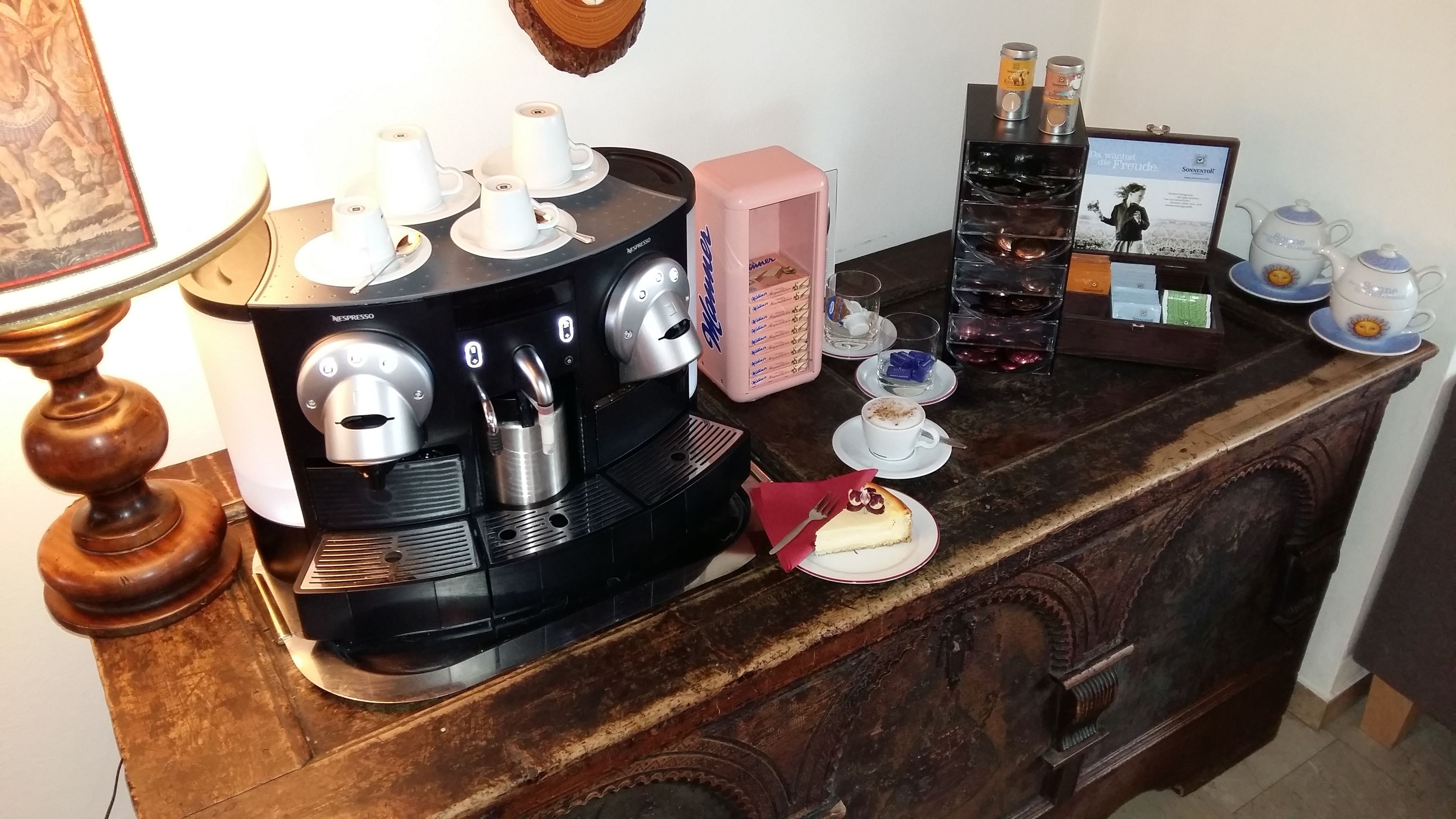 Una macchina da caffè con più tazze, una scatola rosa, un bicchiere d'acqua e una torta su un tavolo di legno.