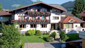 A two-story building with a sign reading "Landhaus Steiner". It has a balcony with flowers, a well-maintained lawn, and a mountain backdrop. - Landhaus Steiner (Altenmarkt im Pongau)