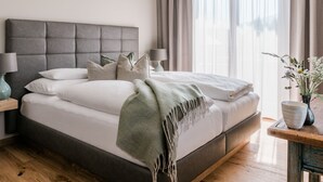 A modern bedroom with a large bed, a bedside table with a lamp, and a window with curtains. - Landhaus Steiner (Altenmarkt im Pongau)