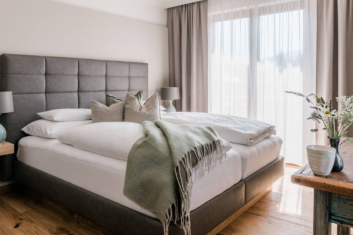 A modern bedroom with a large bed, a bedside table with a lamp, and a window with curtains.
