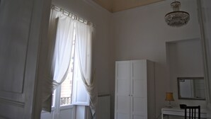 A room with a large window, white curtains, a white wardrobe, a desk with a lamp, and a mirror. - A Casa di Giuseppe (Palermo)