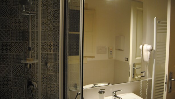 A bathroom with patterned tiles, a sink, a mirror, and a hairdryer. - A Casa di Giuseppe (Palermo)
