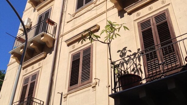 A multi-story building with balconies, windows with shutters, and some potted plants. - A Casa di Giuseppe (Palermo)