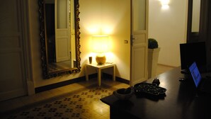 A hotel room with a large ornate mirror, a small table with a lamp, a computer on a desk, and a decorative bowl. - A Casa di Giuseppe (Palermo)