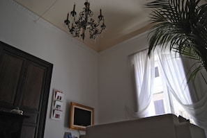 A room with a chandelier, a wooden cabinet, a framed picture, and a window with curtains. - A Casa di Giuseppe (Palermo)