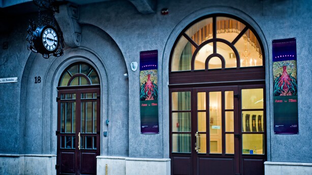 Un edificio con dos puertas arqueadas, un reloj sobre la puerta izquierda y dos carteles en las paredes.