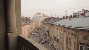 Vista de la calle desde un balcón, con edificios, cielo despejado y algunos vehículos.