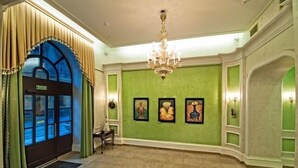 Un amplio vestíbulo con candelabro, paredes verdes y obras de arte enmarcadas.