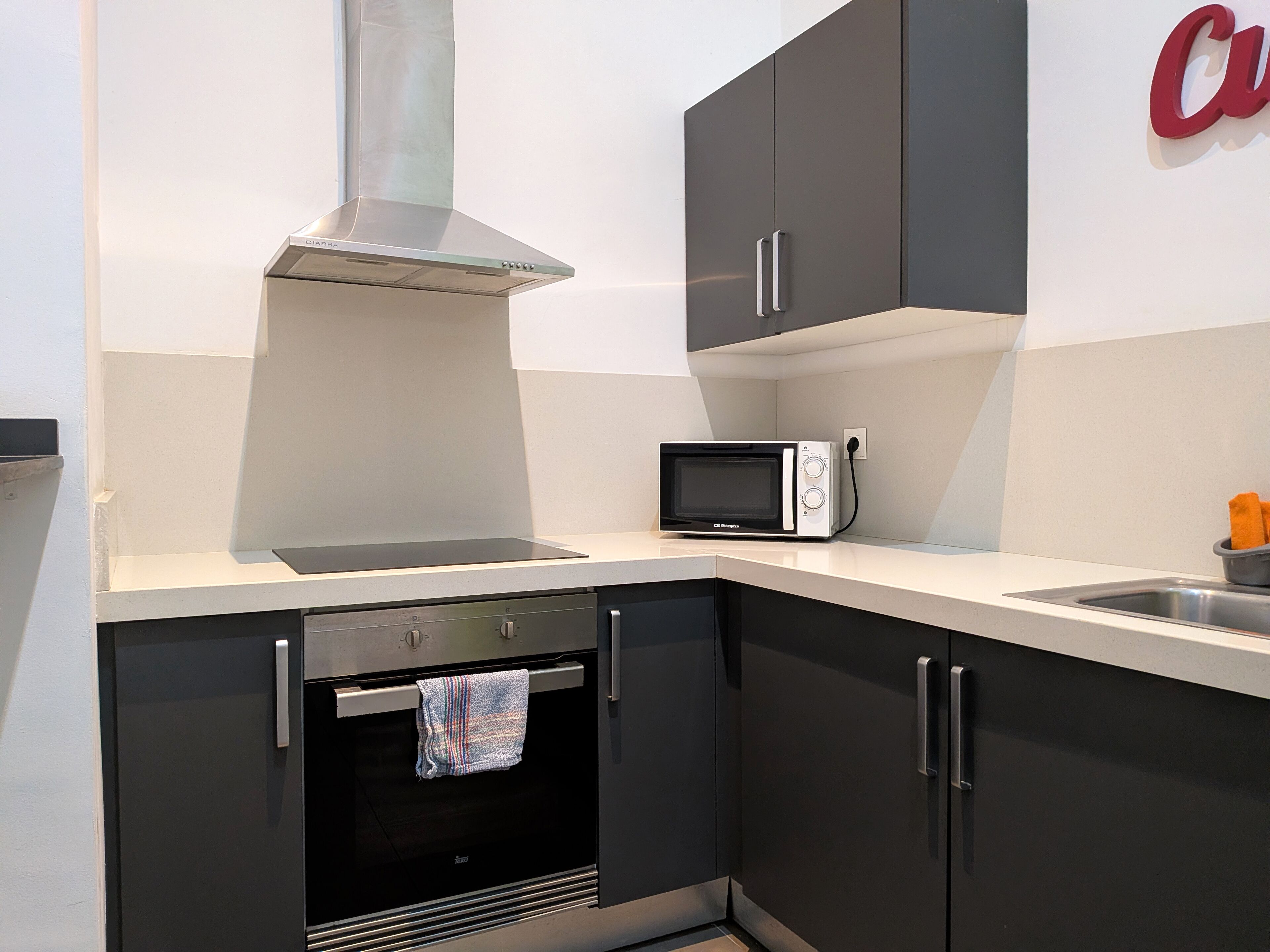 A compact kitchen with a built-in microwave, oven, and stainless steel range hood.