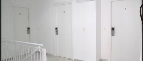Un pasillo con puertas numeradas 15, 16 y 17, cada una con un timbre y un interruptor de luz.