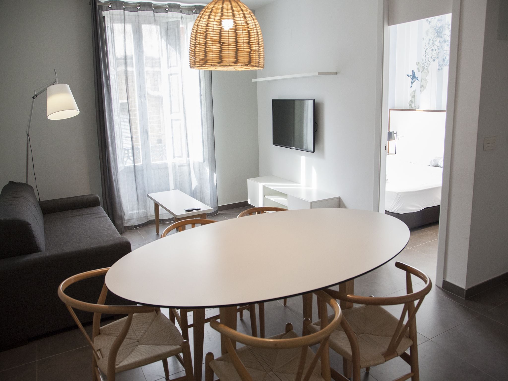 A modern living room with a round dining table, wooden chairs, a sofa, a TV, and a window with curtains.