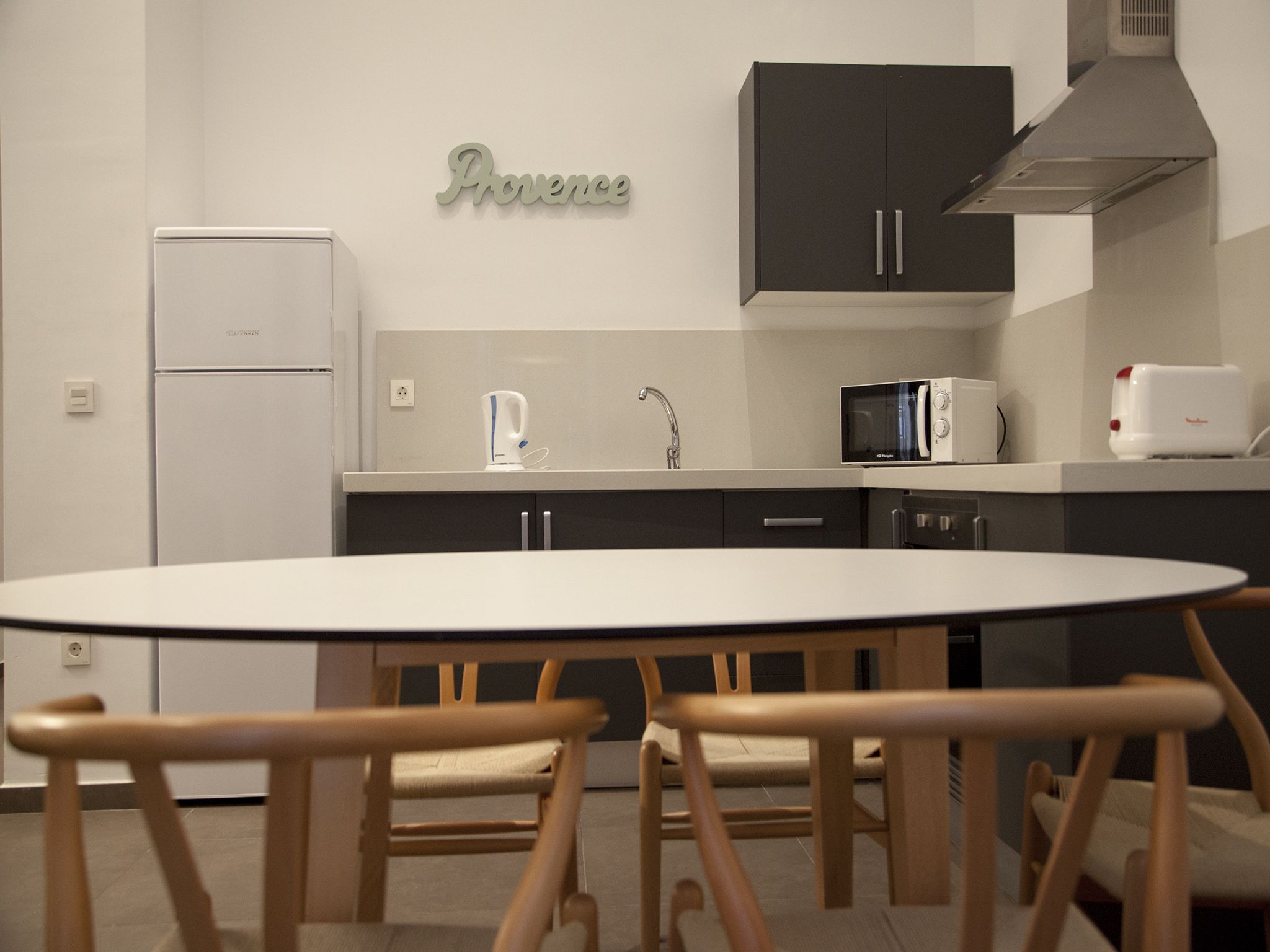 A modern kitchen with a white refrigerator, a coffee maker, a microwave, and a toaster. There is a table with chairs in the center.