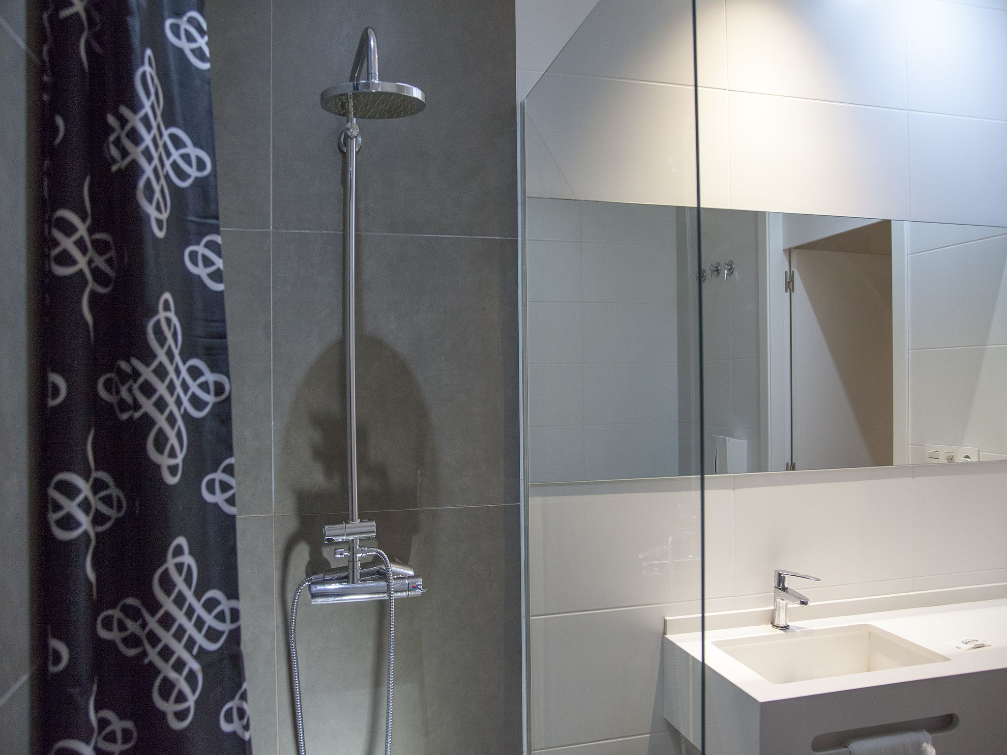 A modern bathroom with a glass shower enclosure, a white sink, and a large mirror.