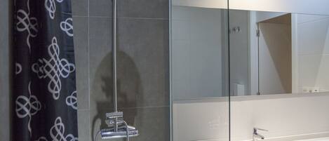 A modern bathroom with a glass shower enclosure, a white sink, and a large mirror.
