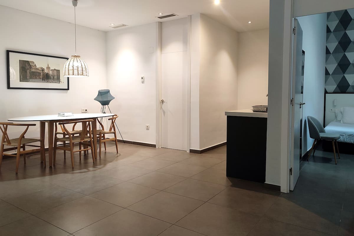 A modern kitchen with white cabinets, a dining area with a white table and wooden chairs, and a small seating area with a blue chair.
